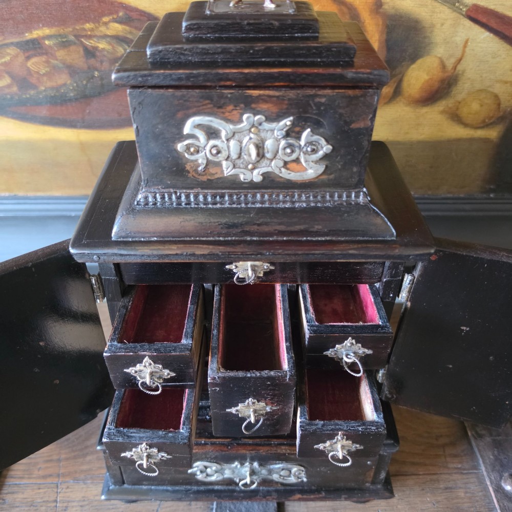 A tiered 18th-century walnut jewellery cabinet featuring ornate silvered metal hinges, a central latch mechanism, a lower drawer, and turned bun feet. View VIII