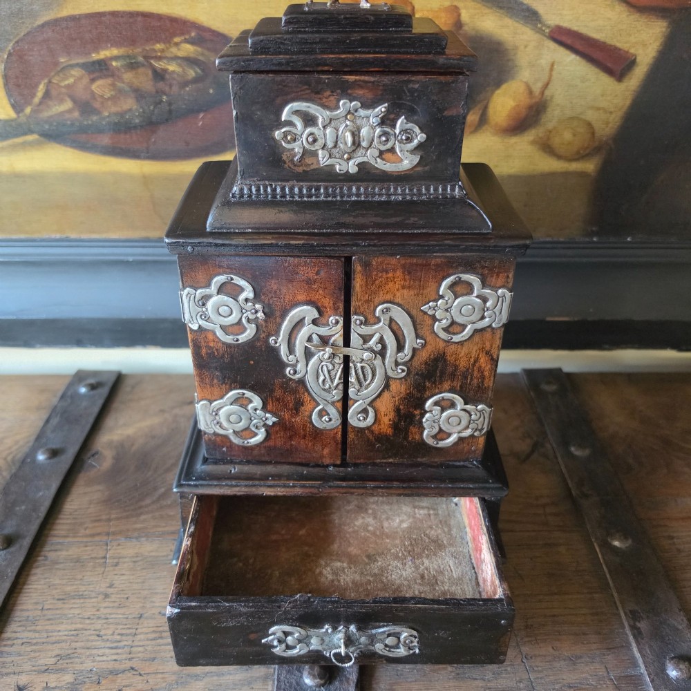 A tiered 18th-century walnut jewellery cabinet featuring ornate silvered metal hinges, a central latch mechanism, a lower drawer, and turned bun feet. View IX