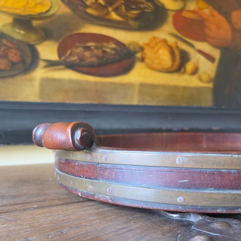 An 18th-century oval mahogany serving tray featuring a raised gallery edge with brass rim binding and carved scroll handles. View II