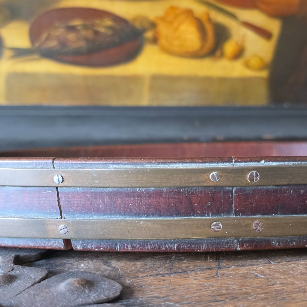 An 18th-century oval mahogany serving tray featuring a raised gallery edge with brass rim binding and carved scroll handles. View III