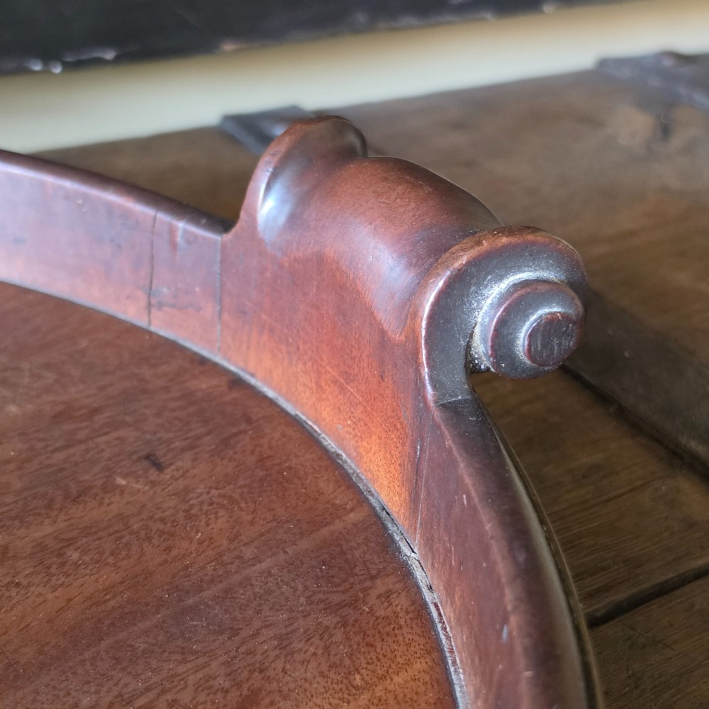 An 18th-century oval mahogany serving tray featuring a raised gallery edge with brass rim binding and carved scroll handles. View IV