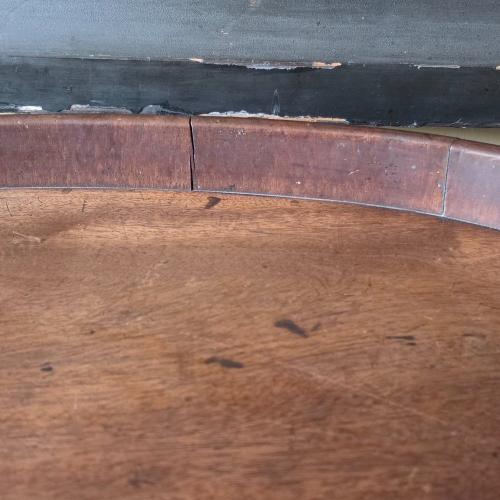 An 18th-century oval mahogany serving tray featuring a raised gallery edge with brass rim binding and carved scroll handles. View V