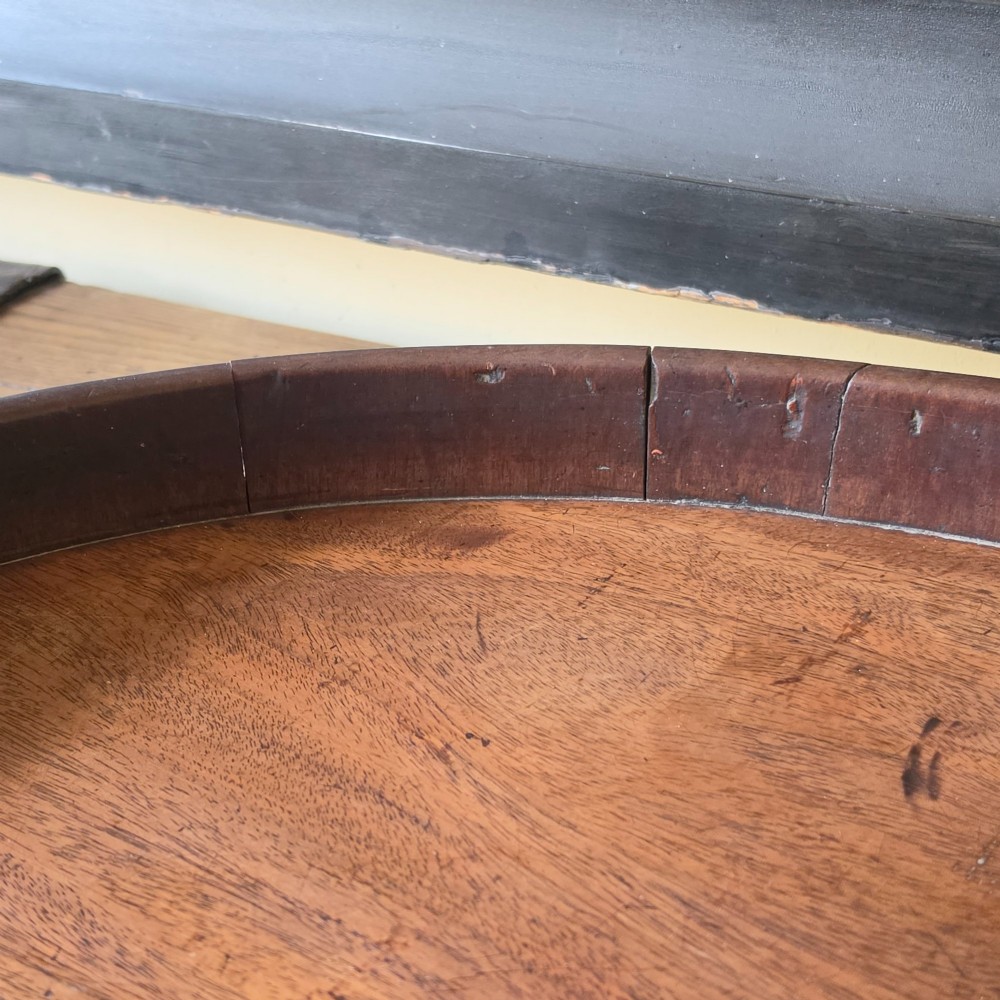 An 18th-century oval mahogany serving tray featuring a raised gallery edge with brass rim binding and carved scroll handles. View VI