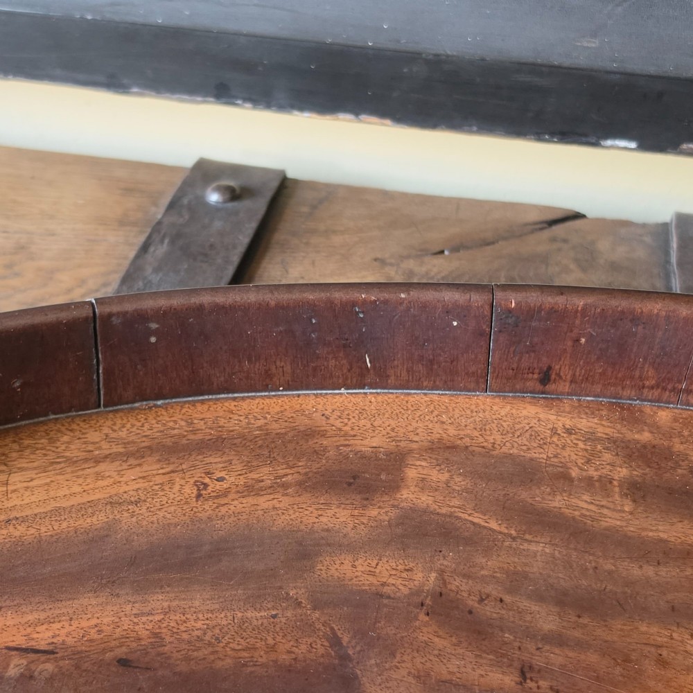 An 18th-century oval mahogany serving tray featuring a raised gallery edge with brass rim binding and carved scroll handles. View VII