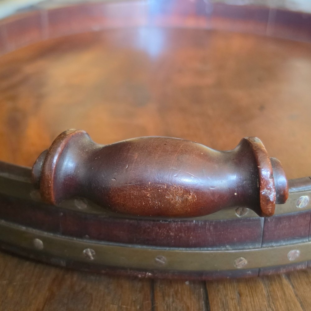 An 18th-century oval mahogany serving tray featuring a raised gallery edge with brass rim binding and carved scroll handles. View IX