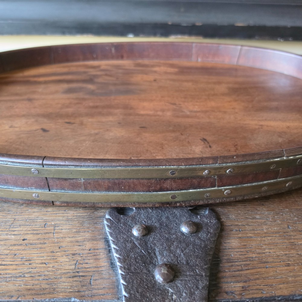 An 18th-century oval mahogany serving tray featuring a raised gallery edge with brass rim binding and carved scroll handles. View XI