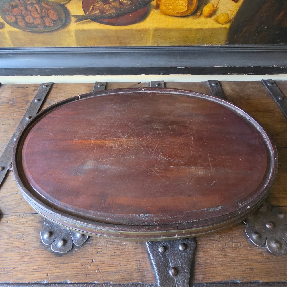An 18th-century oval mahogany serving tray featuring a raised gallery edge with brass rim binding and carved scroll handles. View XII