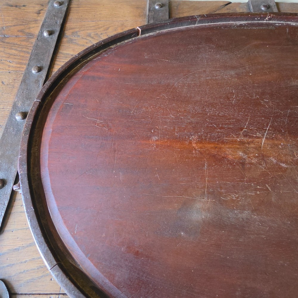 An 18th-century oval mahogany serving tray featuring a raised gallery edge with brass rim binding and carved scroll handles. View XIII