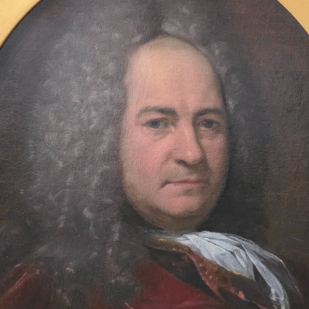 An 18th-century oil portrait of a gentleman in a grey wig and red coat, presented in an oval aperture within a rectangular giltwood frame. View II