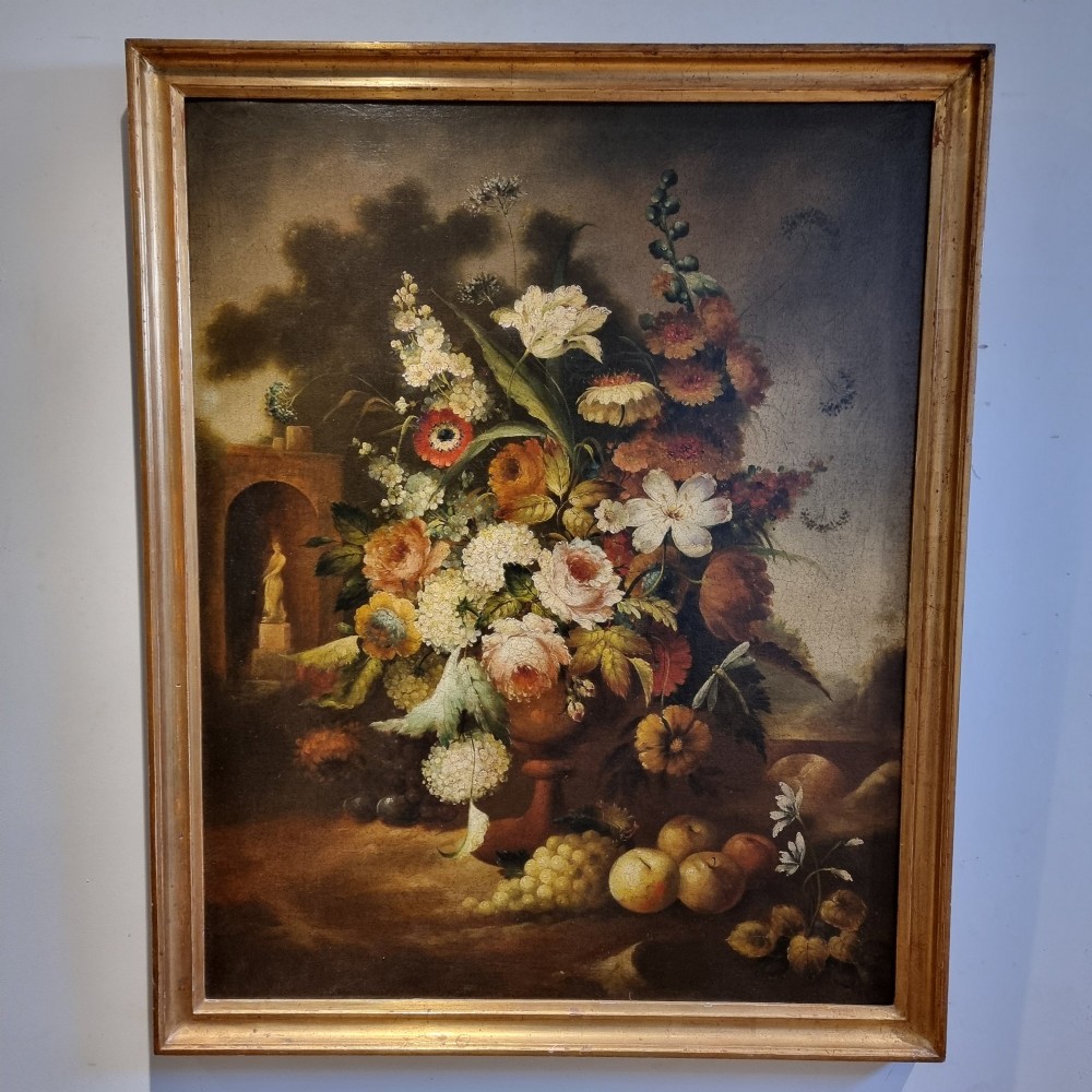 An 18th-century style oil painting on canvas depicting a floral arrangement in an urn with fruit at the base, housed within a gilded wooden frame.