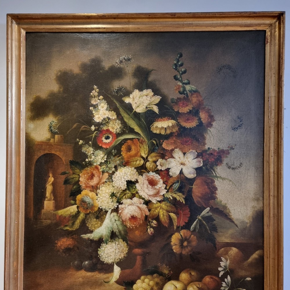 An 18th-century style oil painting on canvas depicting a floral arrangement in an urn with fruit at the base, housed within a gilded wooden frame. View II