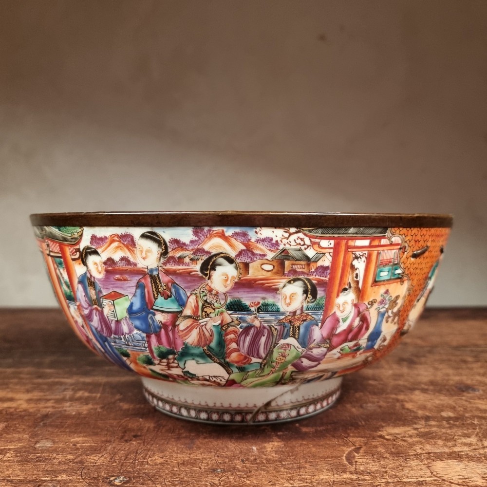 A 19th-century Chinese porcelain bowl featuring hand-painted polychrome figural scenes and a metal-bound rim.