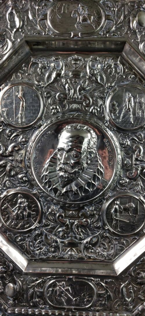 An octagonal nineteenth-century silvered metal charger featuring relief repousse decoration depicting a central portrait bust of Miguel de Cervantes surrounded by narrative vignettes and foliate scrollwork. View V