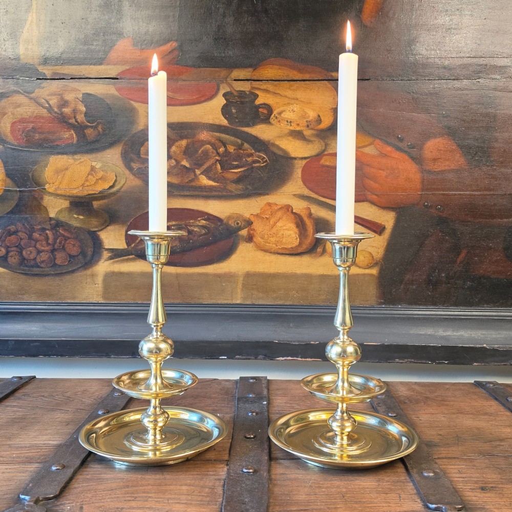 A pair of 19th-century turned brass candlesticks featuring wide circular drip pans and stepped bases.