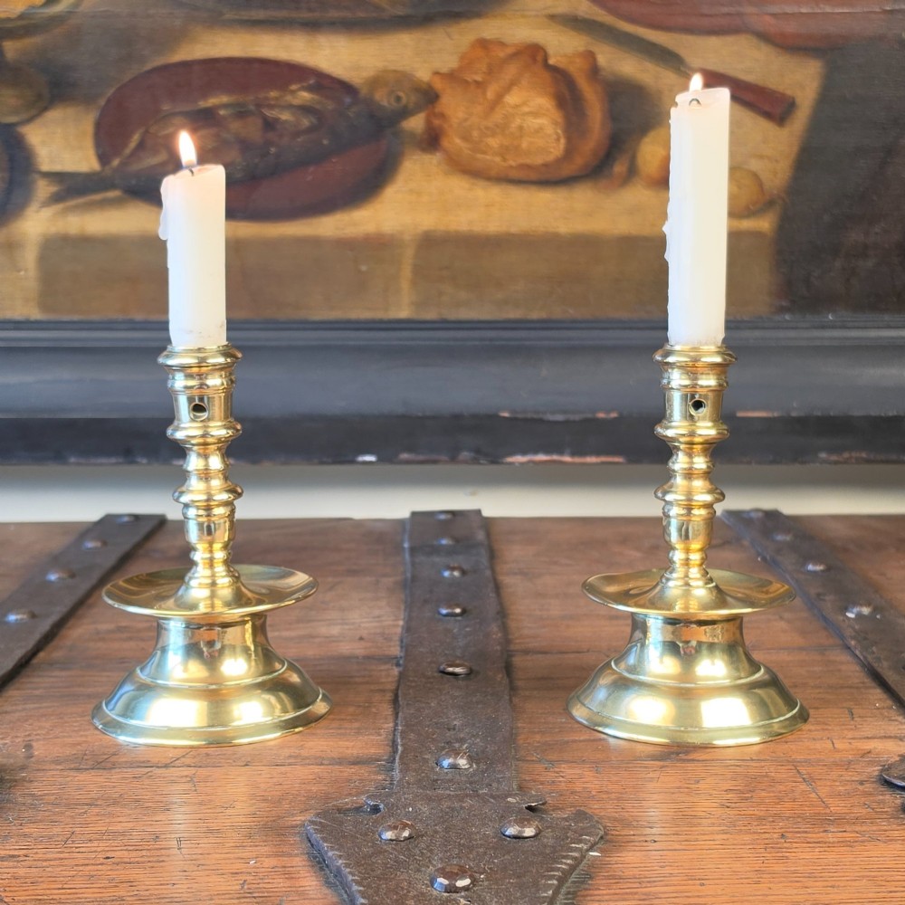 A pair of small turned brass candlesticks featuring flared circular bases, baluster stems, and sockets with wax removal holes.