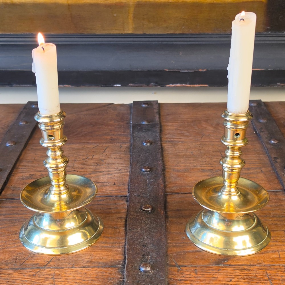 A pair of small turned brass candlesticks featuring flared circular bases, baluster stems, and sockets with wax removal holes. View II