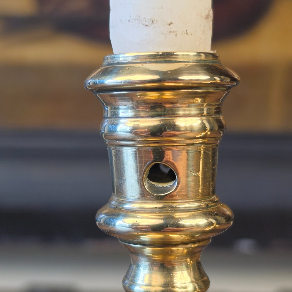 A pair of small turned brass candlesticks featuring flared circular bases, baluster stems, and sockets with wax removal holes. View V
