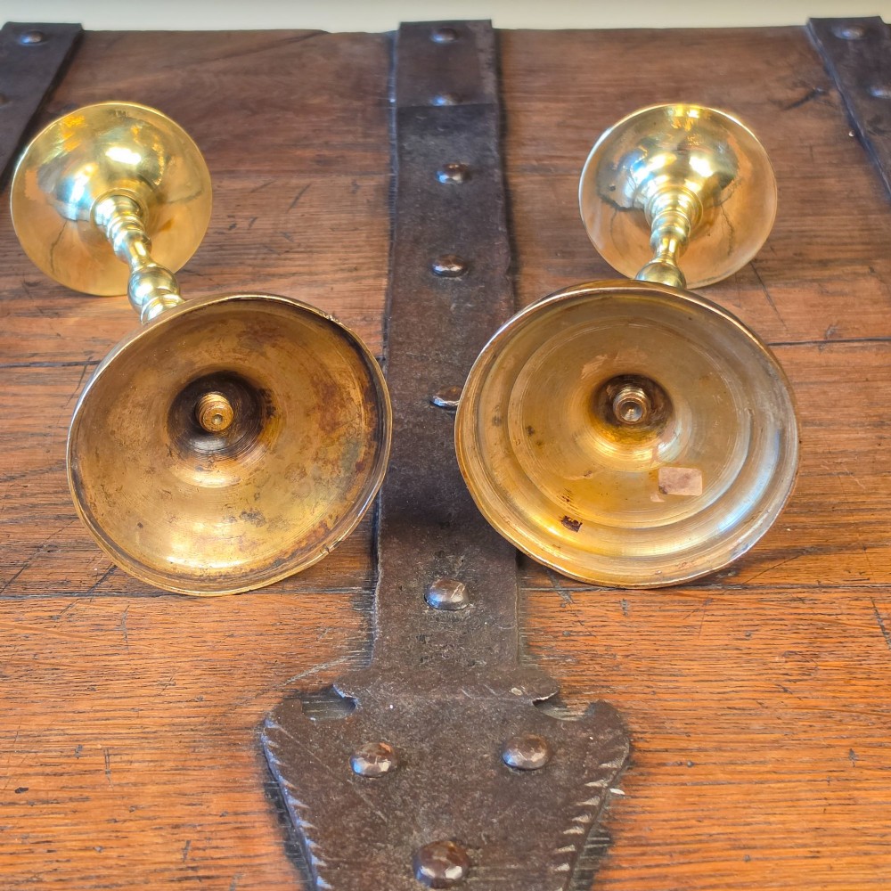 A pair of turned brass pricket candlesticks with circular drip pans and central sharp spikes on stepped round bases. View IV