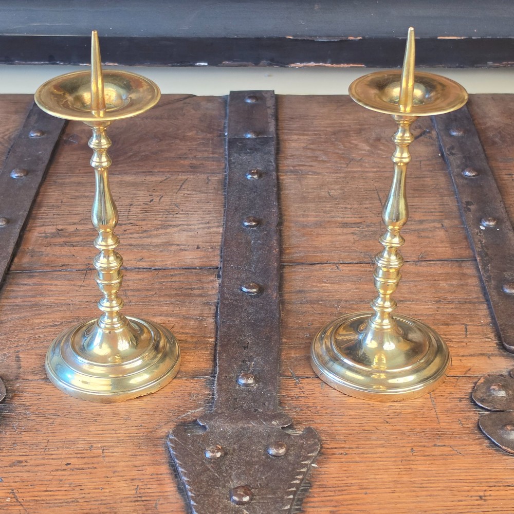 A pair of turned brass pricket candlesticks with circular drip pans and central sharp spikes on stepped round bases.