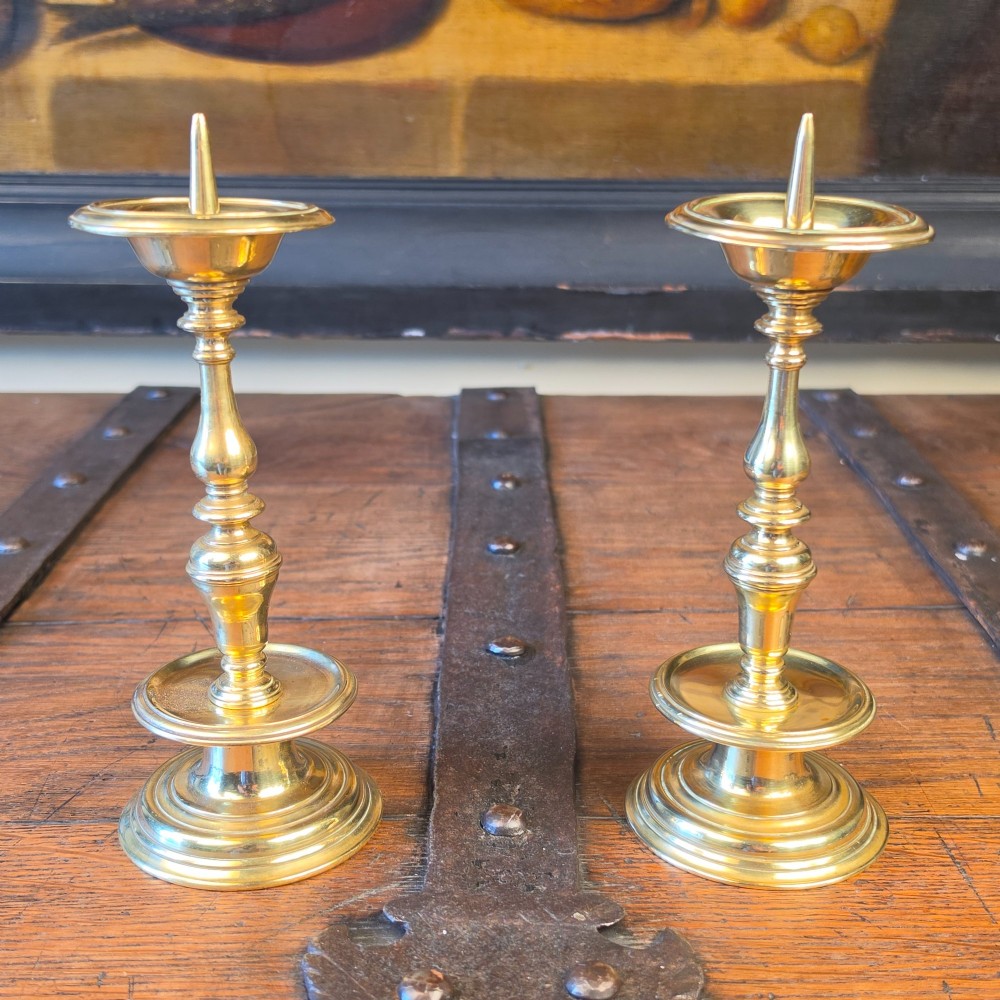 A pair of brass pricket candlesticks featuring central spikes, circular drip pans, baluster-turned stems, and stepped bases.