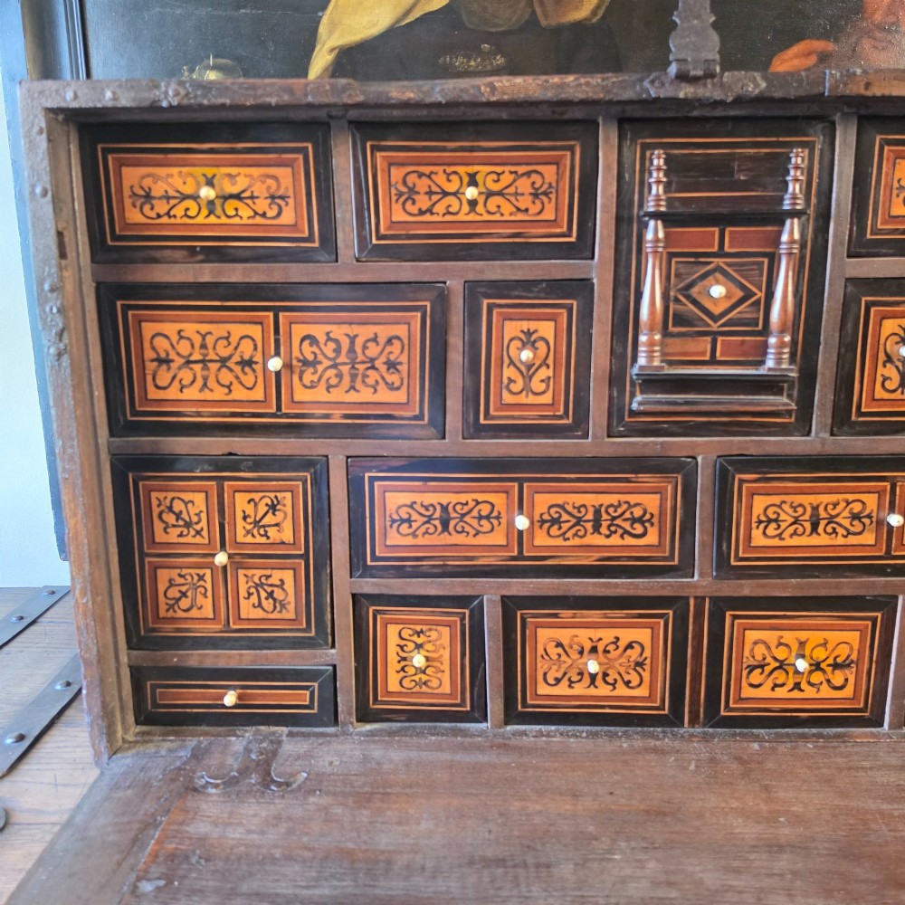 A seventeenth-century dark walnut fall-front table cabinet featuring multiple drawers decorated with intricate geometric and scrollwork wood inlays around an architectural central door. View X