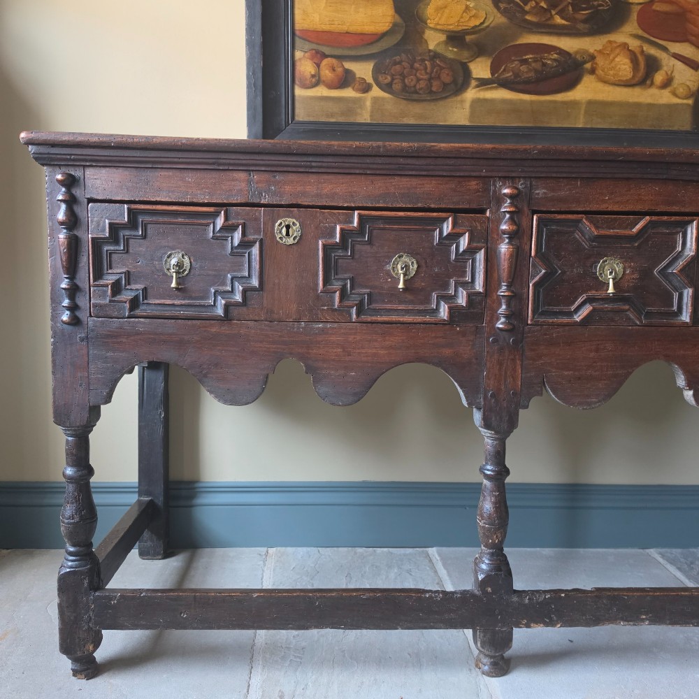 A long 17th-century dark oak dresser base featuring geometric moulded drawers, turned legs, and a shaped apron. View III