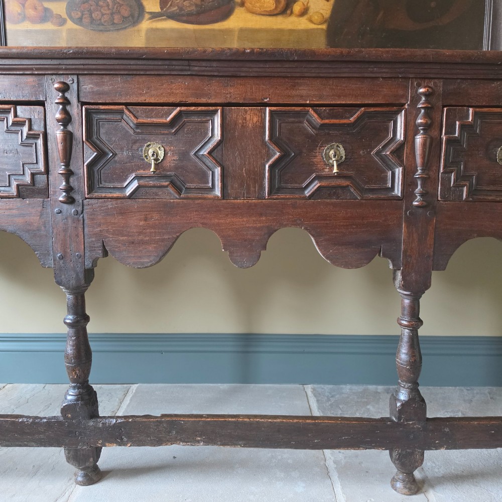 A long 17th-century dark oak dresser base featuring geometric moulded drawers, turned legs, and a shaped apron. View IV