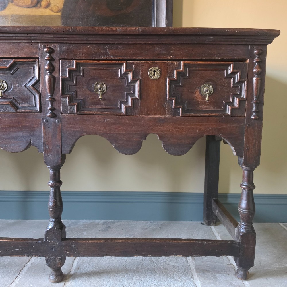 A long 17th-century dark oak dresser base featuring geometric moulded drawers, turned legs, and a shaped apron. View V
