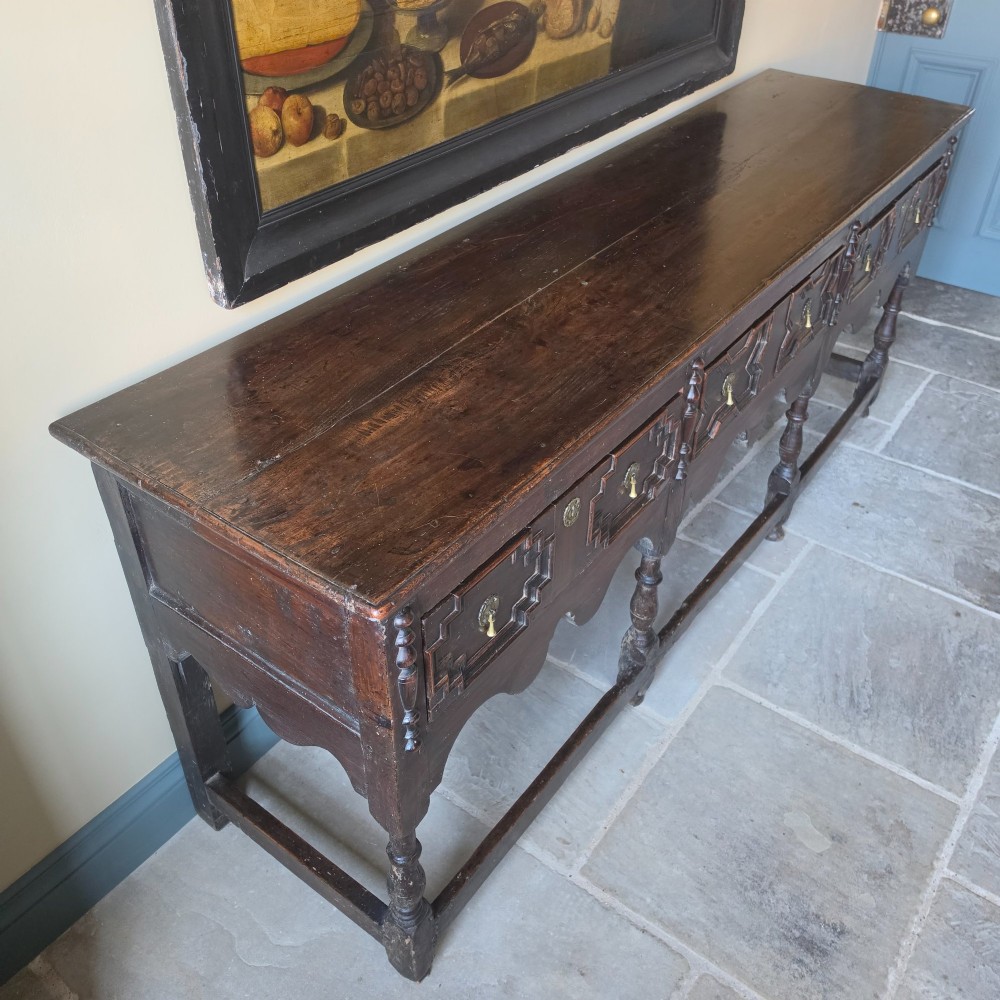 A long 17th-century dark oak dresser base featuring geometric moulded drawers, turned legs, and a shaped apron. View XI