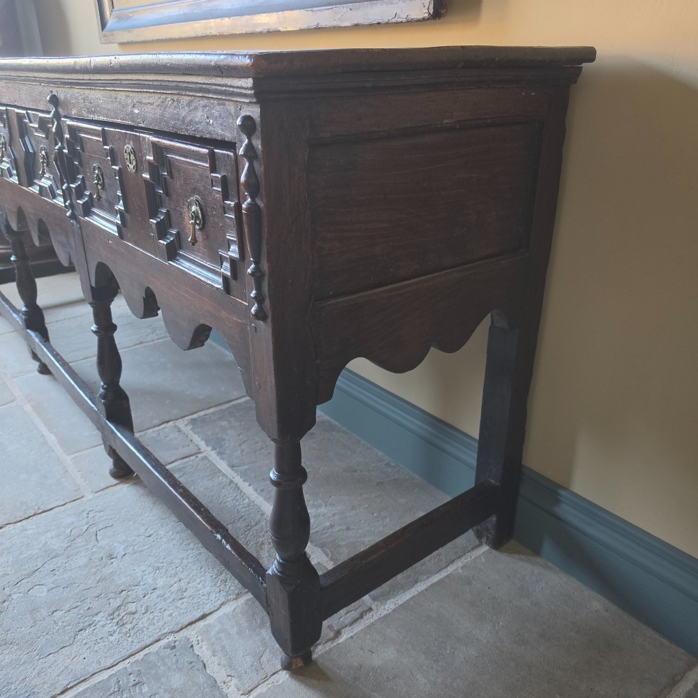 A long 17th-century dark oak dresser base featuring geometric moulded drawers, turned legs, and a shaped apron. View XIII