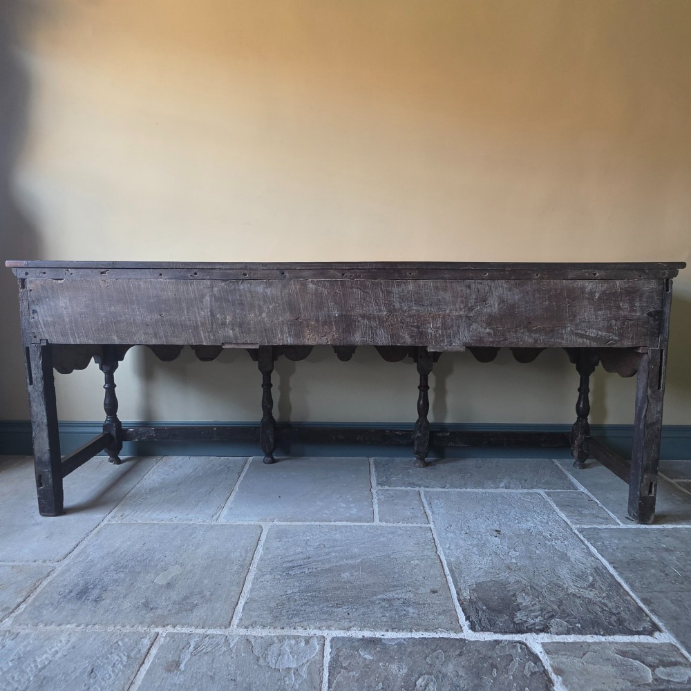 A long 17th-century dark oak dresser base featuring geometric moulded drawers, turned legs, and a shaped apron. View XIV