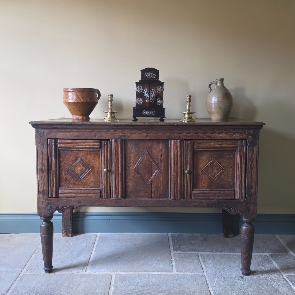 A 17th century dark oak food hutch with carved diamond lozenge doors and turned front legs.