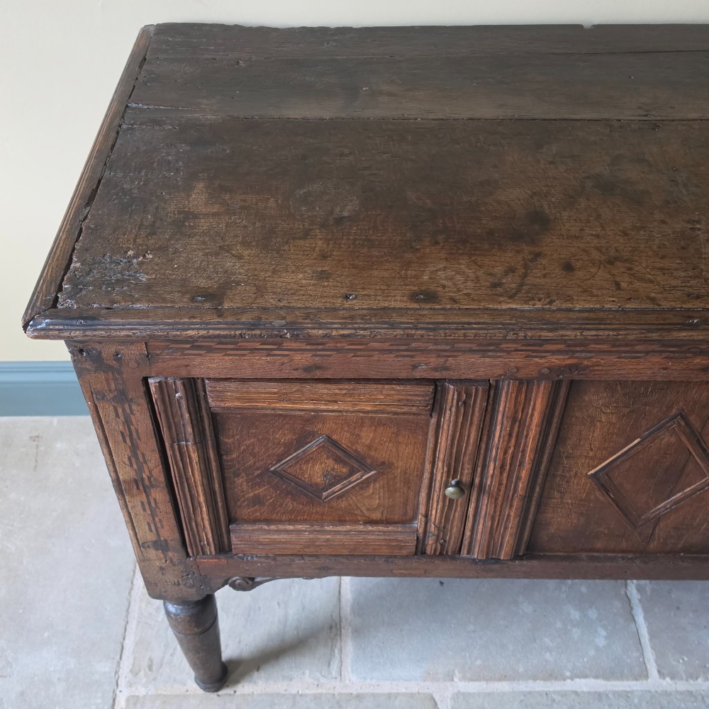 A 17th century dark oak food hutch with carved diamond lozenge doors and turned front legs. View IV