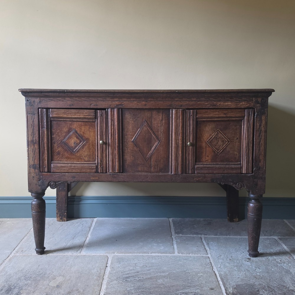 A 17th century dark oak food hutch with carved diamond lozenge doors and turned front legs. View II