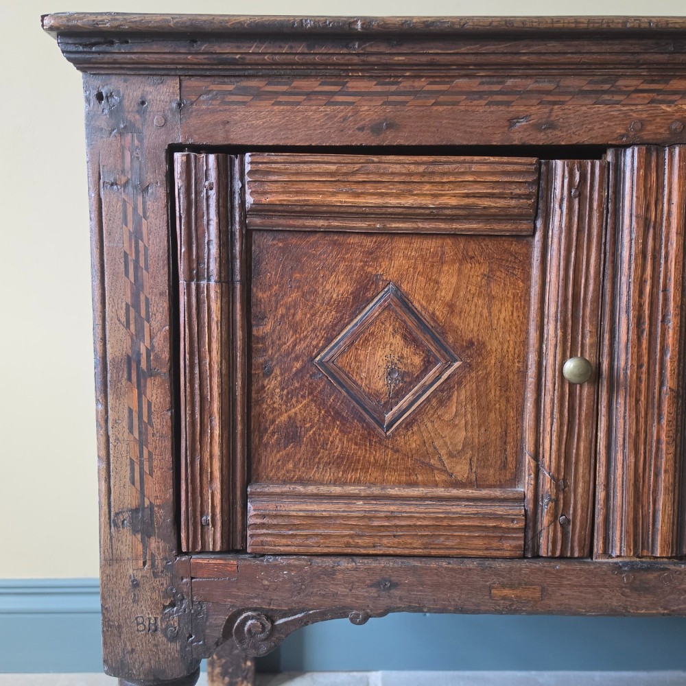 A 17th century dark oak food hutch with carved diamond lozenge doors and turned front legs. View V