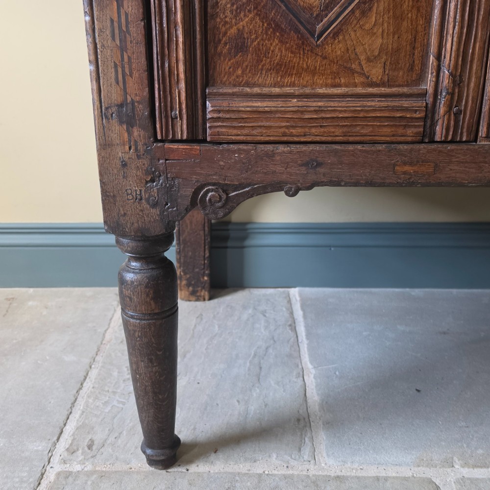 A 17th century dark oak food hutch with carved diamond lozenge doors and turned front legs. View VI