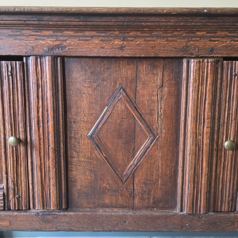 A 17th century dark oak food hutch with carved diamond lozenge doors and turned front legs. View VII