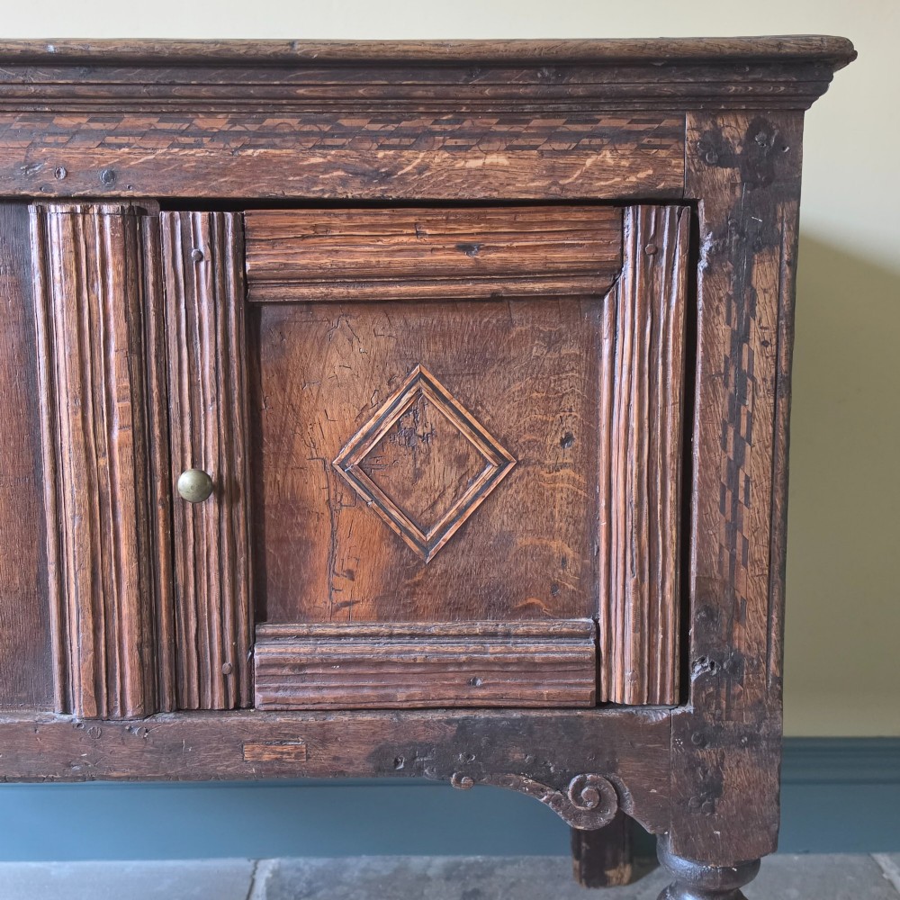 A 17th century dark oak food hutch with carved diamond lozenge doors and turned front legs. View VIII