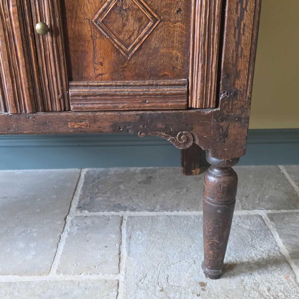 A 17th century dark oak food hutch with carved diamond lozenge doors and turned front legs. View IX
