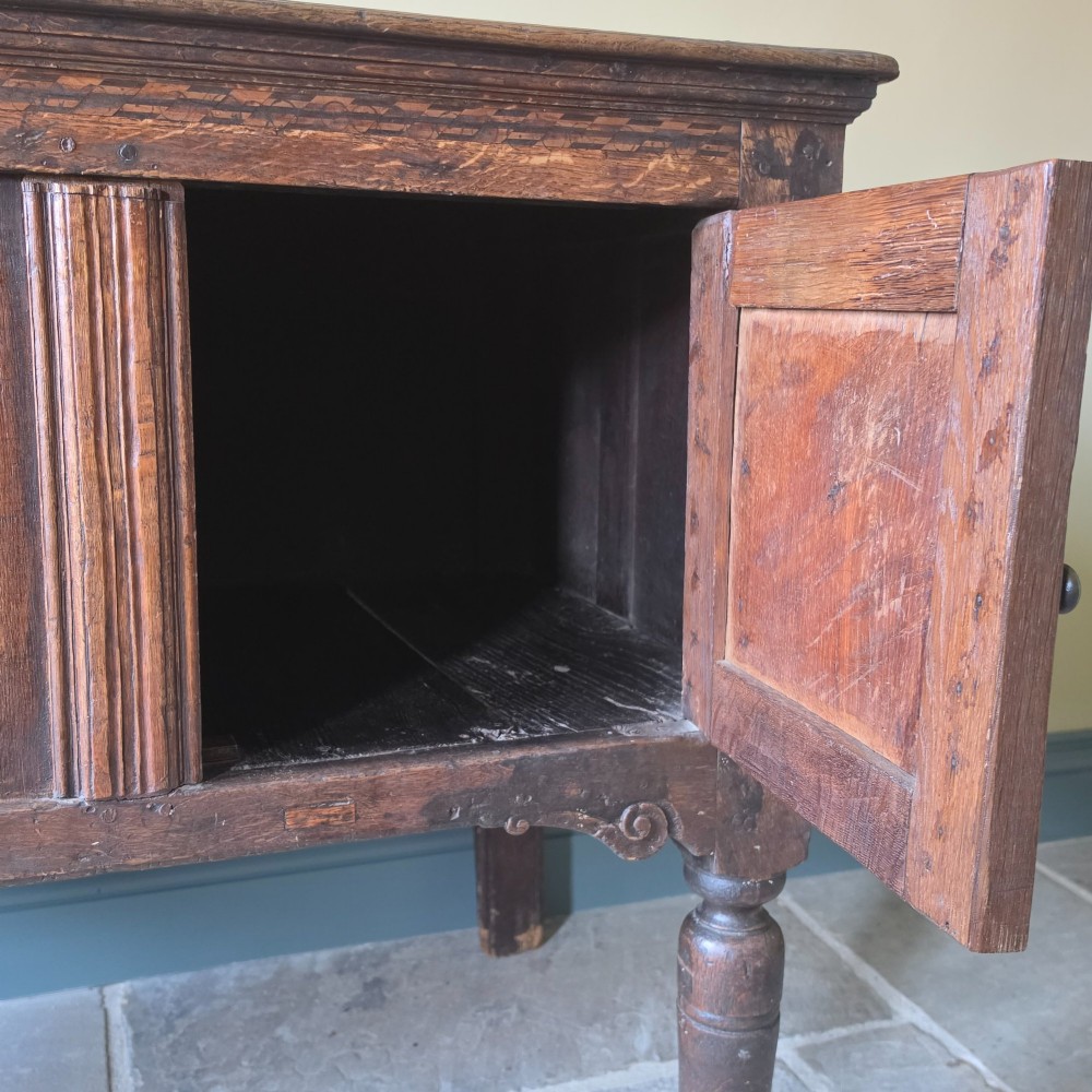A 17th century dark oak food hutch with carved diamond lozenge doors and turned front legs. View X
