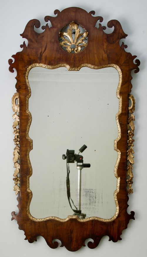 fig 1. A George II walnut wall mirror featuring a shaped fretwork frame, parcel-gilded mouldings, and a carved crest motif.