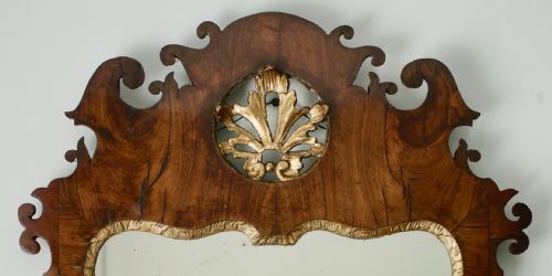 fig 2. A George II walnut wall mirror featuring a shaped fretwork frame, parcel-gilded mouldings, and a carved crest motif.