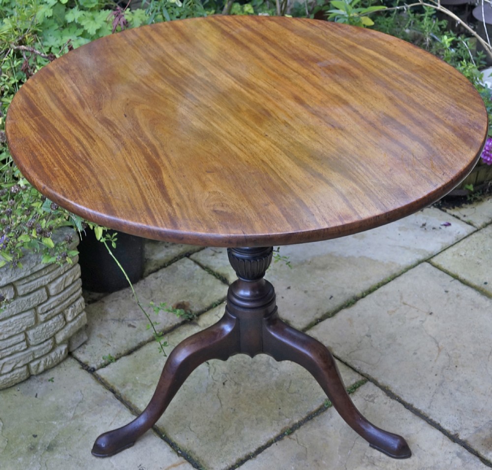 A Georgian mahogany tripod table featuring a circular top, turned carved column, and three cabriole legs.