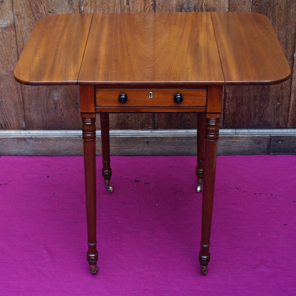 A Regency period mahogany side table featuring two drop flaps, a single drawer with two dark turned knobs, and four ring-turned legs on brass castors. View V