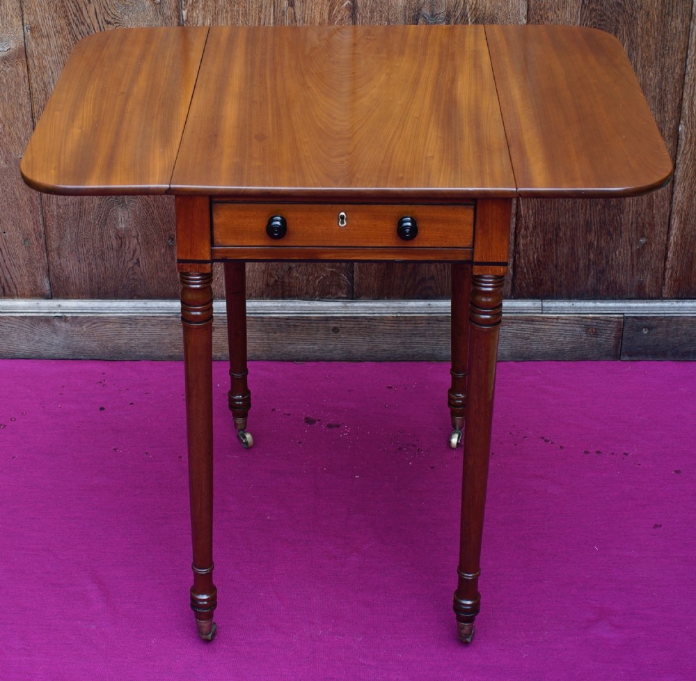 A Regency period mahogany side table featuring two drop flaps, a single drawer with two dark turned knobs, and four ring-turned legs on brass castors.