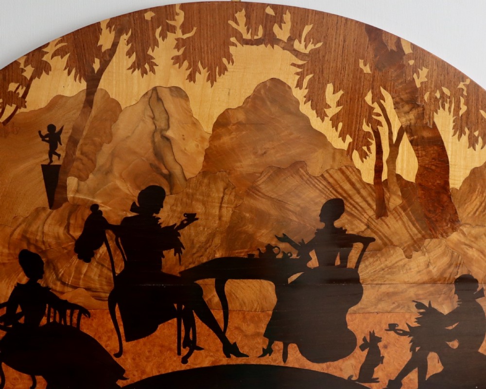 A semi-circular wooden panel featuring intricate marquetry depicting silhouettes of figures taking tea outdoors in a landscape setting. View II
