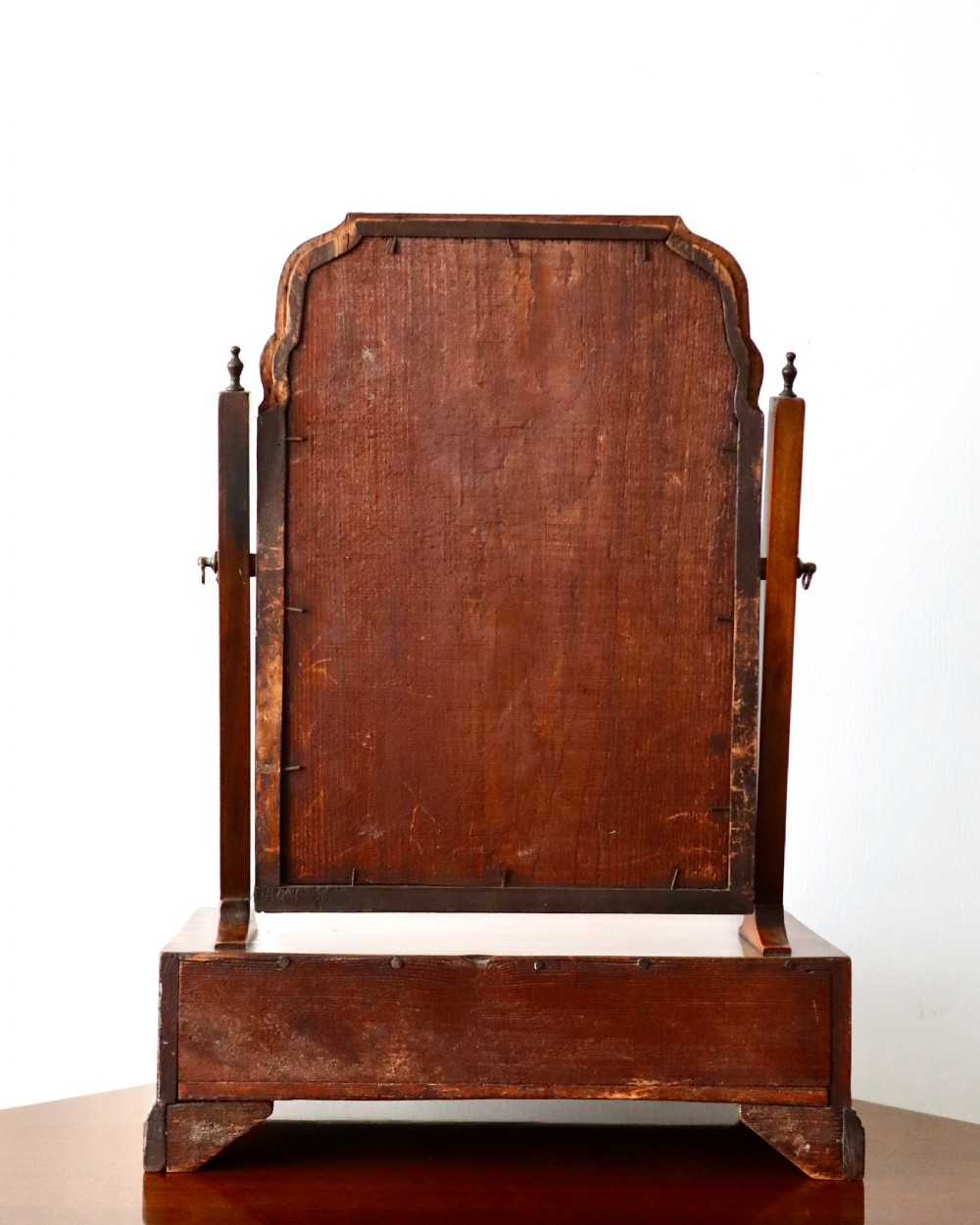 A walnut tabletop toilet mirror featuring an arched swing frame with turned finials mounted above a plinth base containing three small drawers with brass knobs. View IV