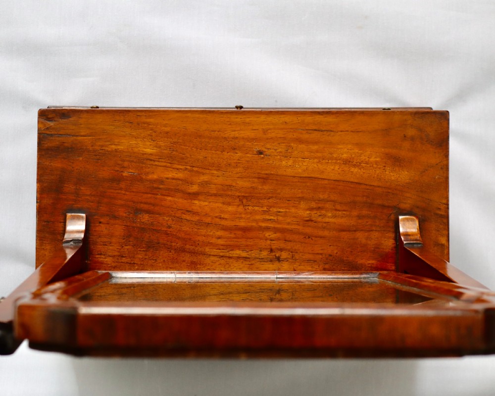 A walnut tabletop toilet mirror featuring an arched swing frame with turned finials mounted above a plinth base containing three small drawers with brass knobs. View V