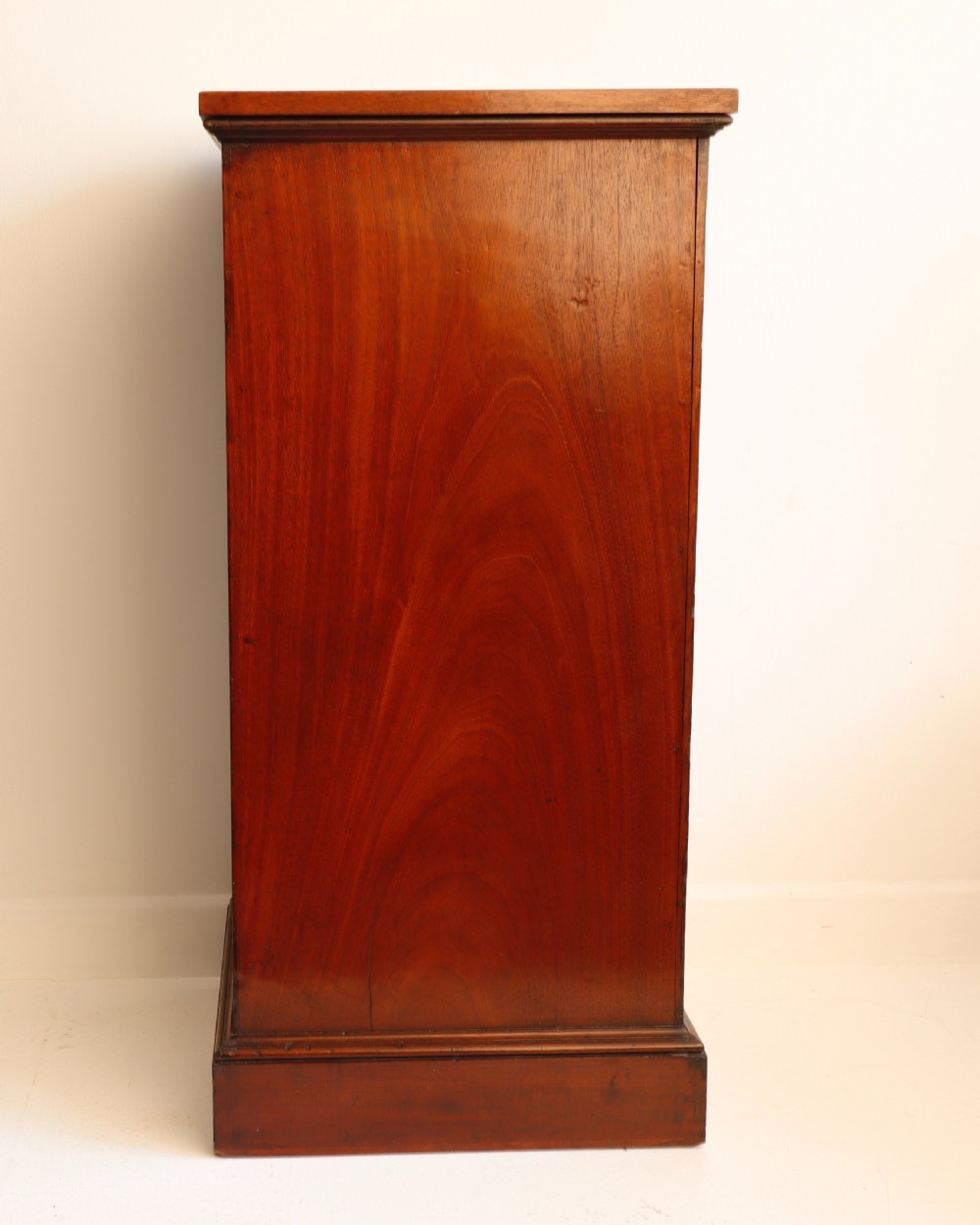 A tall antique flame mahogany cellarette cabinet styled as a chest with three faux drawer fronts, turned wooden knobs, and a solid plinth base. View VIII