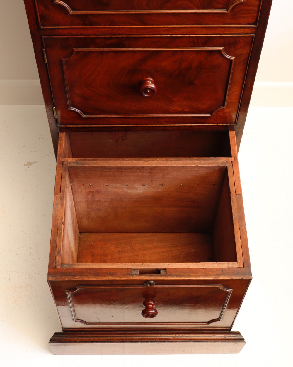 A tall antique flame mahogany cellarette cabinet styled as a chest with three faux drawer fronts, turned wooden knobs, and a solid plinth base. View XII